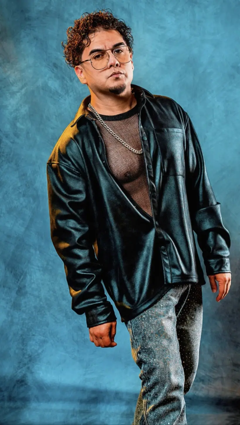 Raél in a black leather shirt against a vivid blue studio backdrop