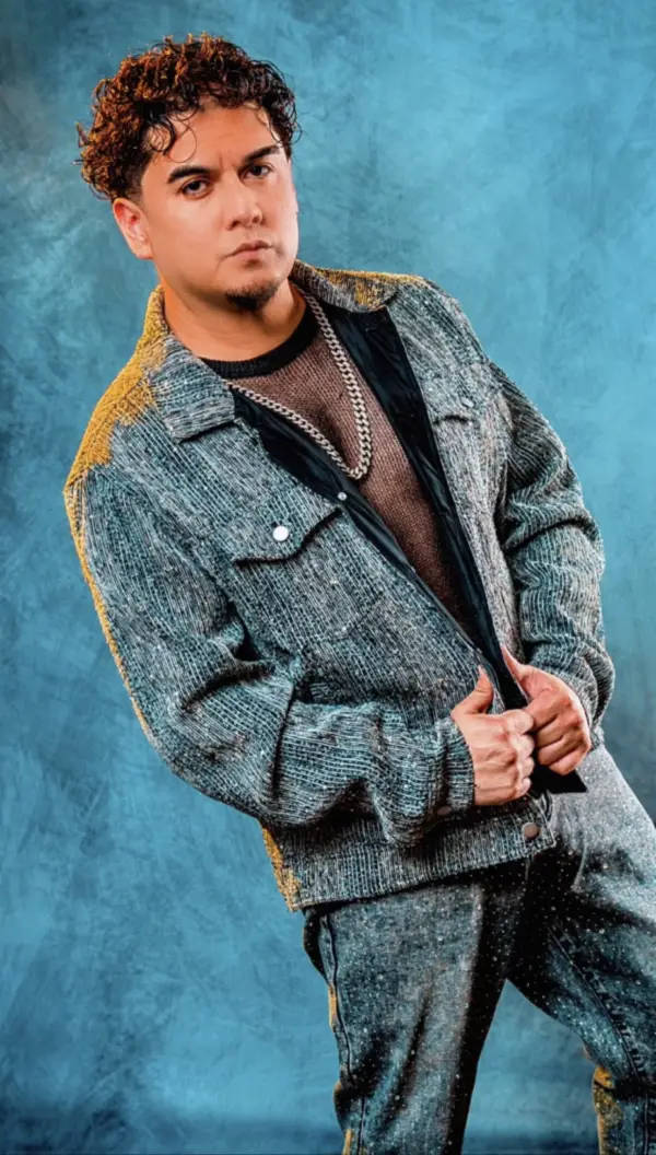 Raél in a textured silver jacket against a vivid blue studio backdrop